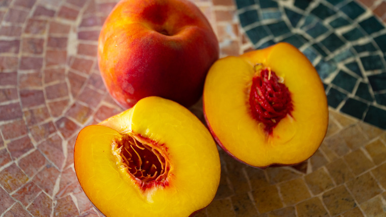 Two peaches on a mosaic table and one split open to show the pit