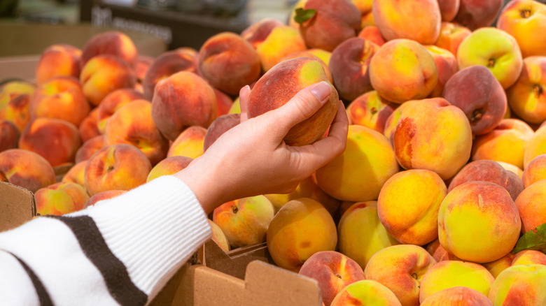Hand grabbing peach from grocery store display tray