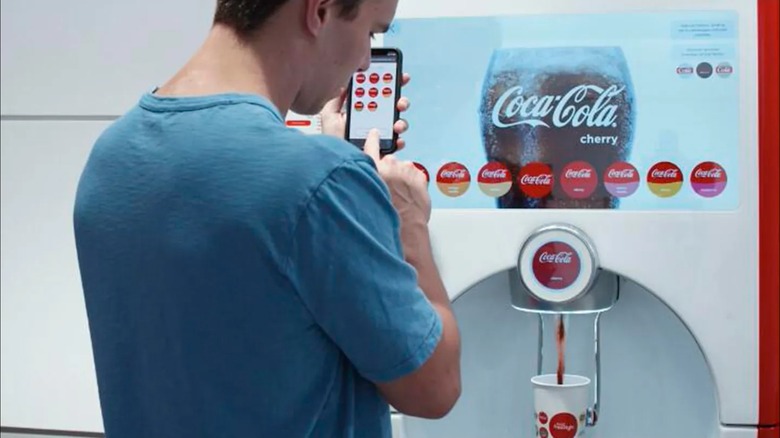 Man selecting options on phone next to coca-cola freestyle machine
