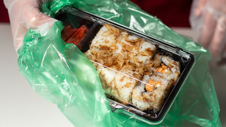 Pieces of suhi being placed in a to-go tray and bag
