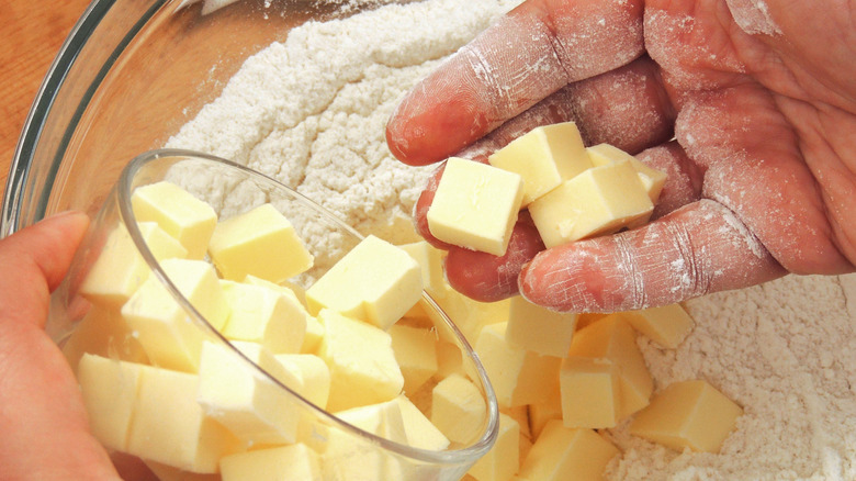 Hands putting butter into flour