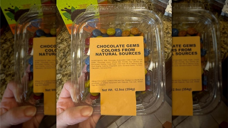 Hand holding plastic, clear container of Sprouts Farmers Market Chocolate Gems