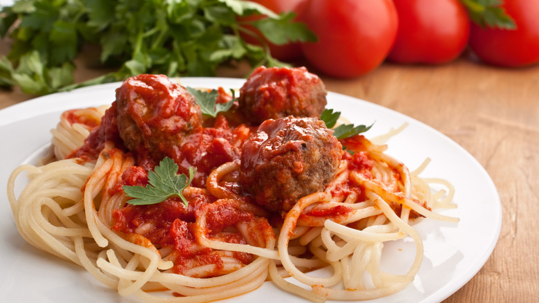 Plate of spaghetti with meatballs in tomato marinara sauce and ingredients on a wooden table.