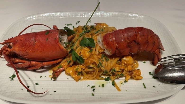 A lobster head and tail arranged around pasta on a rectangular white plate