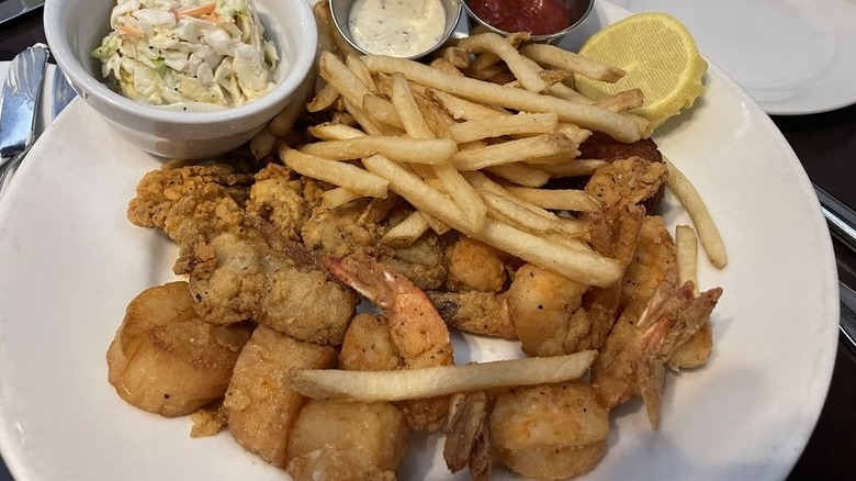 Fried seafood and French fries on a plate with cole slaw, sauces, and half a lemon