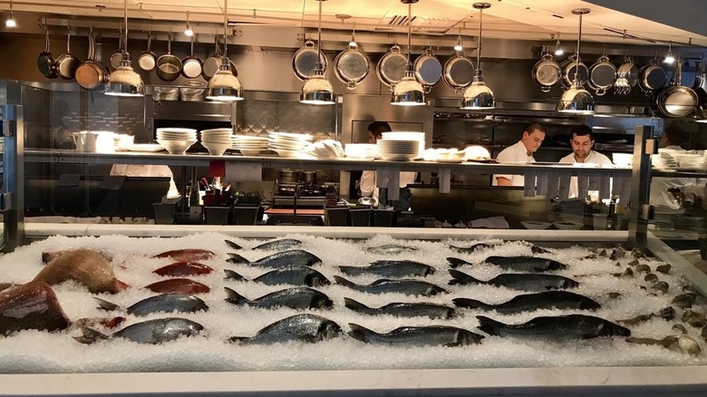 An ice filled display filled with whole fish in front of an open format industrial kitchen at Ostra