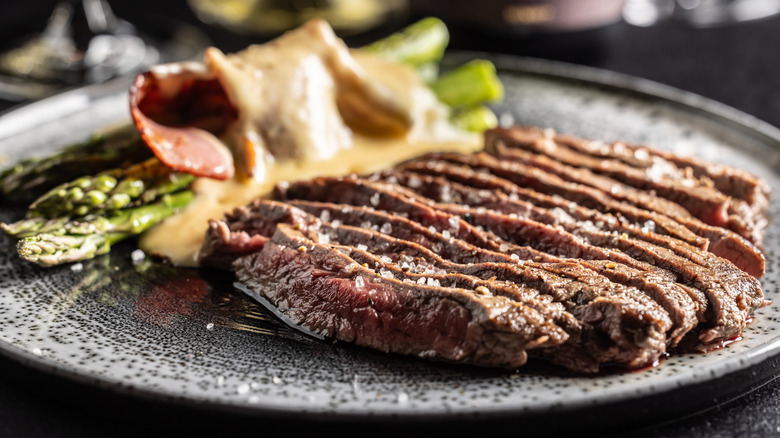 Slices of flank steak on a plate with asparagus and sauce
