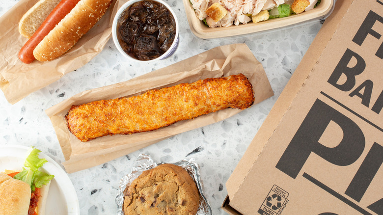 Costco food court items are placed on a table including the chicken bake, hotdog, salad, and pizza box.