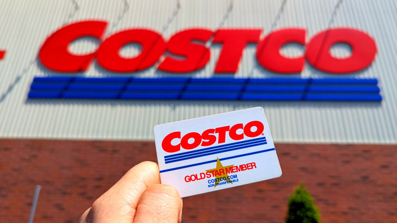 A picture of a Costco card held in front of the Costco sign.