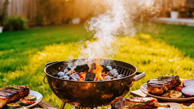 charcoal grill in an outdoor setting shown alongside plates of cooked meat