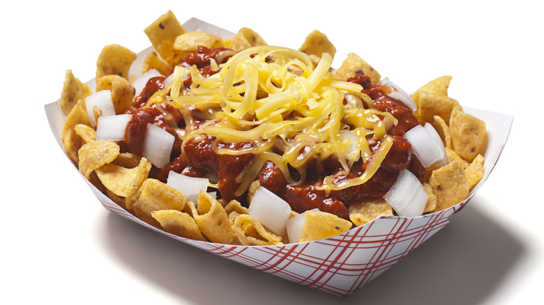 Paper bowl filled with fritos topped with chili and orange cheese against a white background.