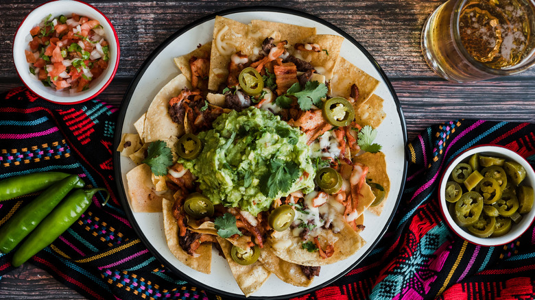 Platter of nachos next to small bowls of pico de gallo and pickled jalapenos.