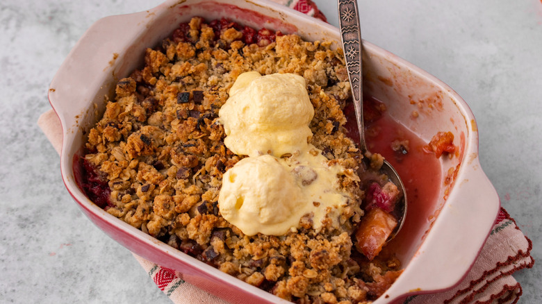 Cobbler baked in a casserole dish with two scoops of vanilla ice cream on it.