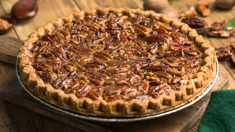 Fresh baked pecan pie in pan resting on wooden cutting board.