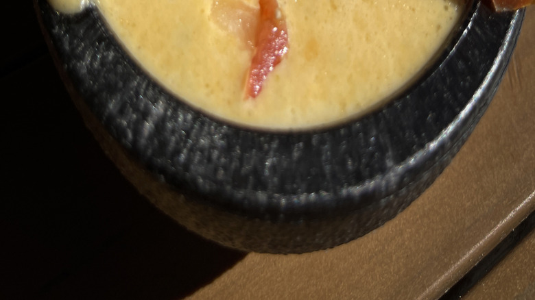 Bowl of melted yellow cheese with diced tomatoes, onion, and peppers.
