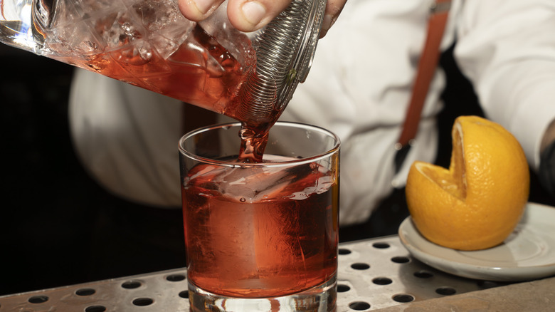 Bartender serves a red cocktail next to an orange missing a wedge