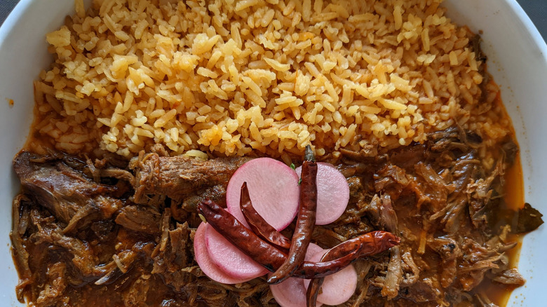 A plate of goat birria with rice and pickled raidshes and dried chile de arbol.