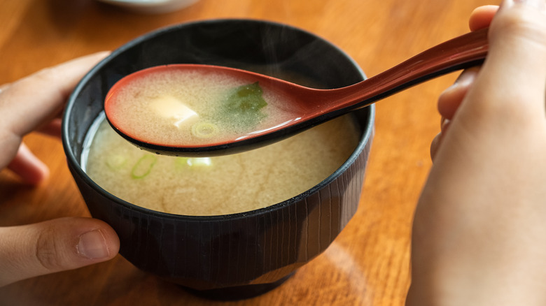 A bowl of miso soup with a spoonful in a person's  hand