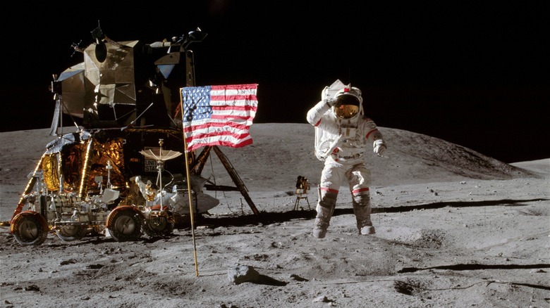 Astronaut on moon next to American flag and lunar rover