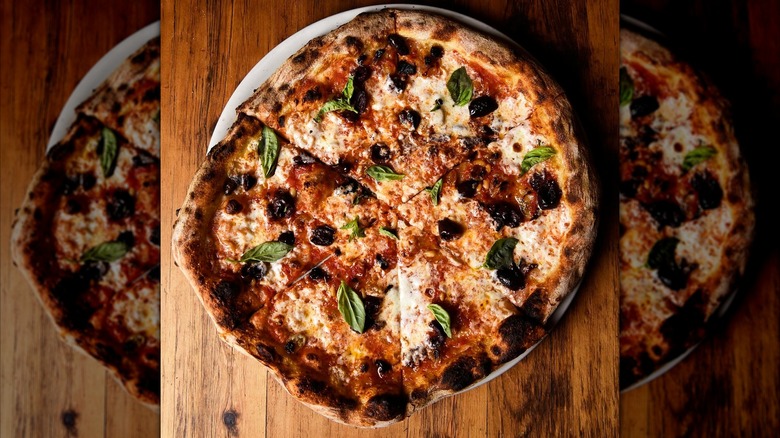 A tomato, mozzarella, and olive pizza with charred crust and fresh basil