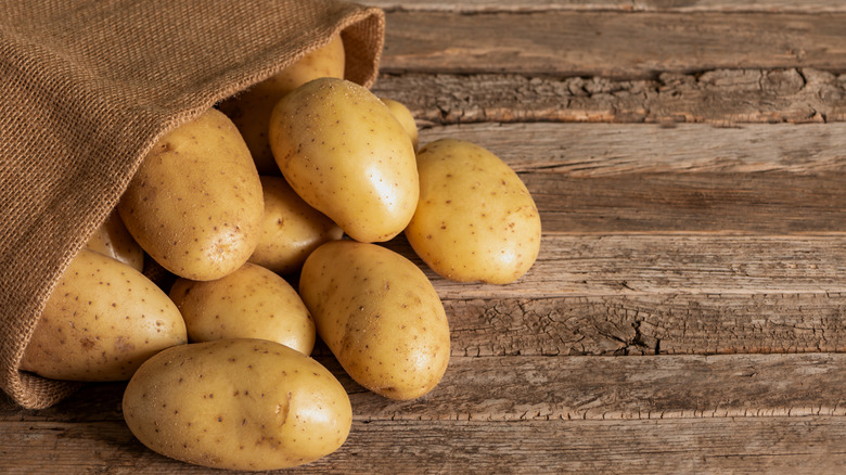 A sack of potatoes spilled over an old wooden table.