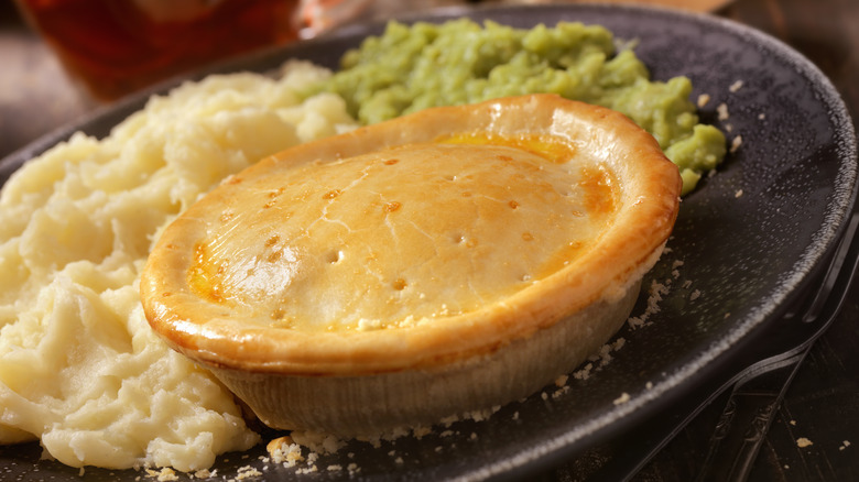 A pot pie served with mashed potatoes and mushy peas