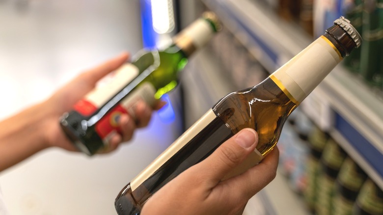 Person holding two beer bottles in front of store shelf
