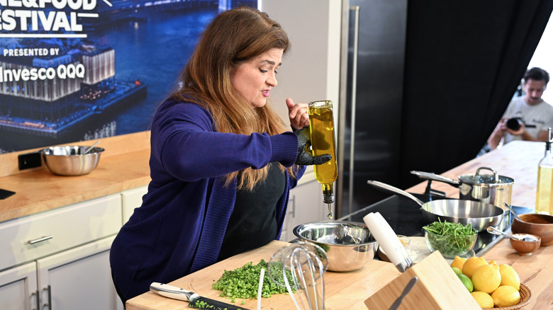 Alex Guarnaschelli pouring olive oil into a pan while on a cooking show.