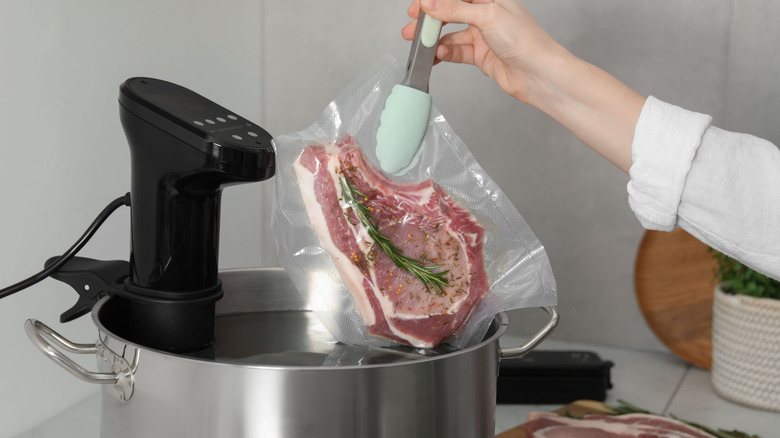 Placing a sealed bag with steak into pot with a sous vide machine.