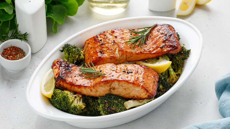 Two salmon filets on a bed of broccoli with lemon wedges and rosemary