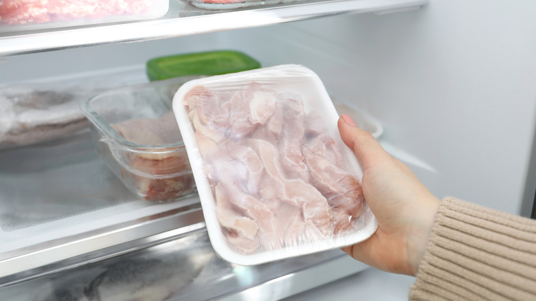 A person holds a package of meat by the fridge