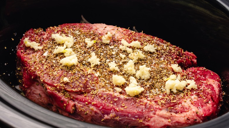 Beef in slow cooker with garlic and seasonings on top
