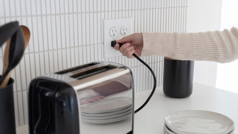 Plugging in a toaster into an electrical outlet in the kitchen.
