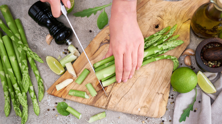 Person's hands cutting the tough ends off asparagus spears on a wooden cutting board
