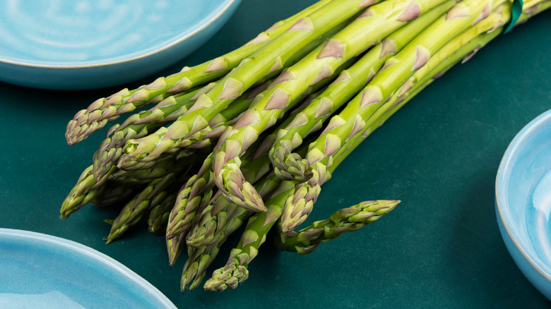 A bunch of fresh raw asparagus with some pale blue dishes