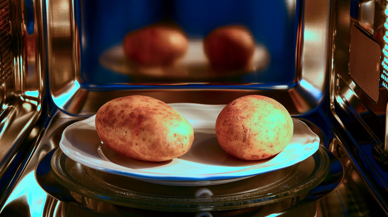 Two baked potatoes on a white plate inside a microwave