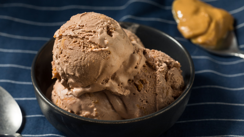 Scoops of chocolate ice cream in a black bowl with a tablespoon of melted peanut butter behind it