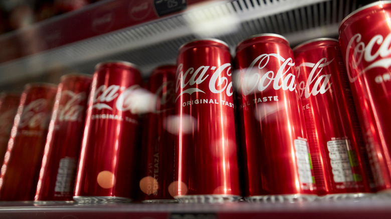 Red cans of Coca-Cola lined up in a refrigerated display case