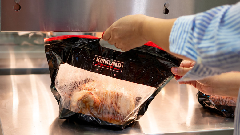 A hand reaching for a Costco rotisserie chicken