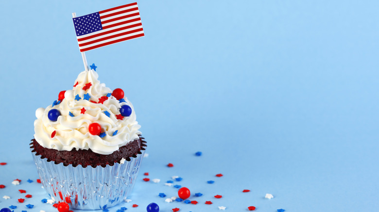 Chocolate cupcake with red, white, and blue sprinkles and small American flag on blue background