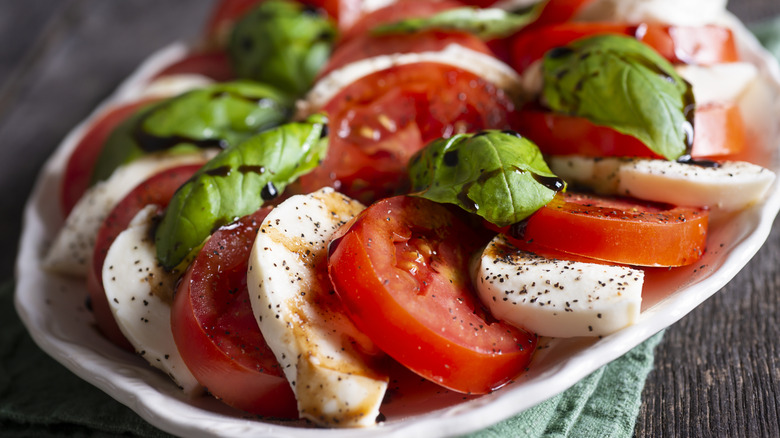 A plate of caprese salad with tomatoes, mozzarella cheese, basil, and balsamic vinegar