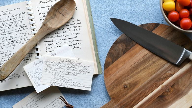 A wooden spoon lays on top of a handwritten recipe book with two recipe cards on top of it