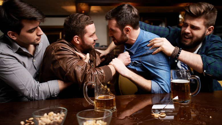 Two men arguing at a bar while other men try to break the fight apart