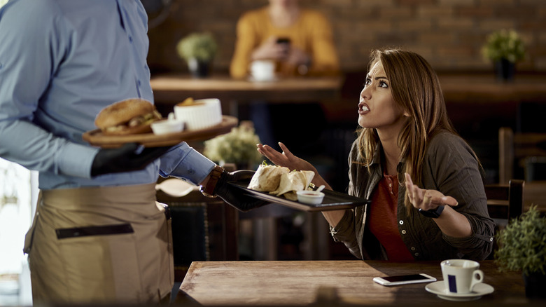 Woman looking angry at server while they hold plates of food