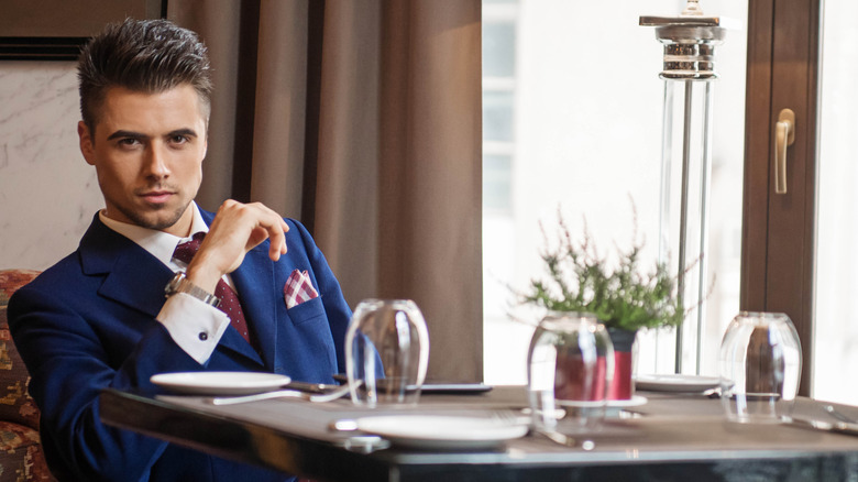 Handsome guy in suit sitting at table with wine glass giving mysterious look