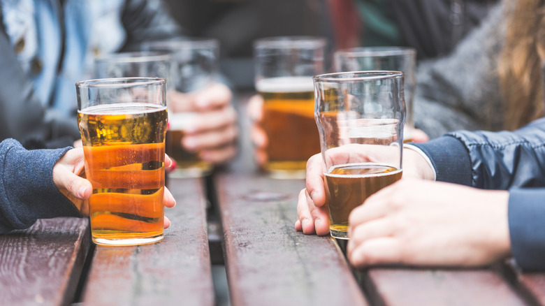 Glasses of beer being held by people sitting at a table outside.