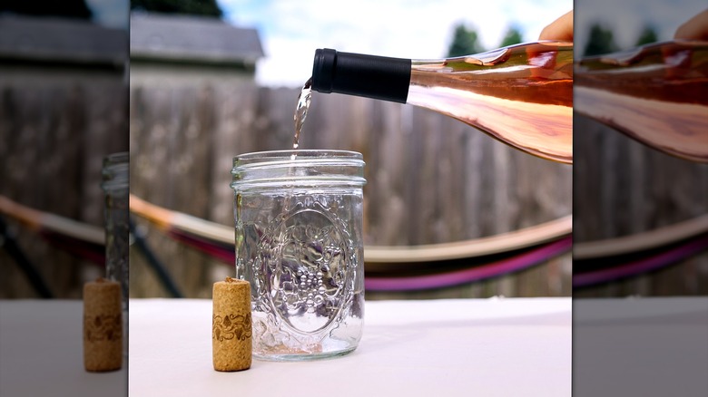 Pouring a bottle of rose wine into a glass Mason jar