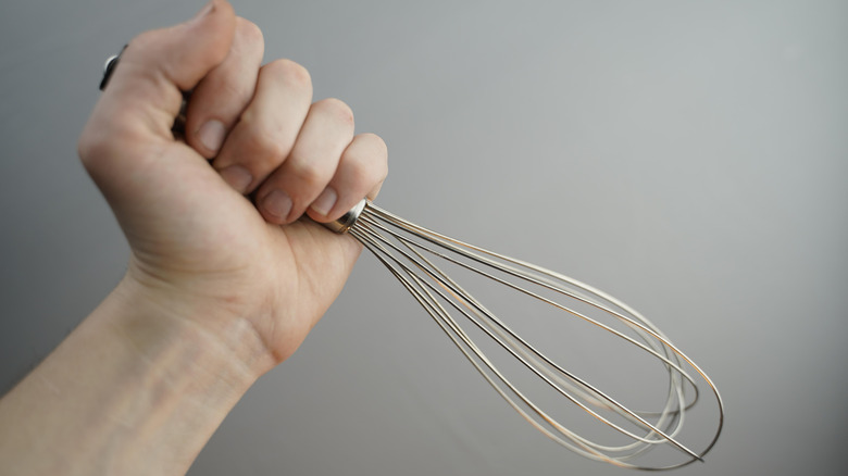 A hand holding a metal kitchen whisk.