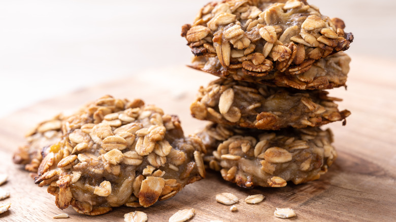 Four banana-oatmeal cookies with a few oats beside them.