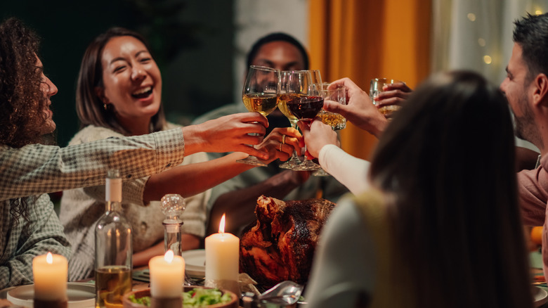 Joyful group of friends raise wine glasses together in toast over candelit dinner table